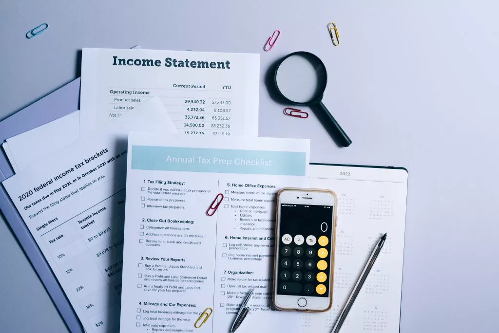 tax documents, a magnifying glass, and a phone on the calculator app